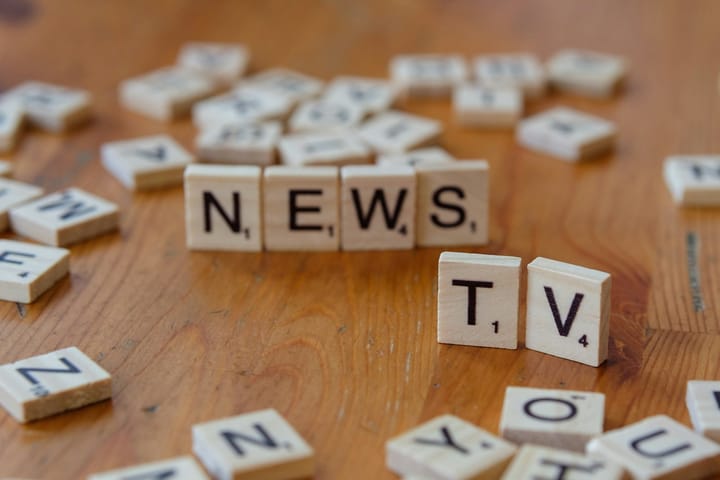 A wooden table topped with scrabble tiles spelling news